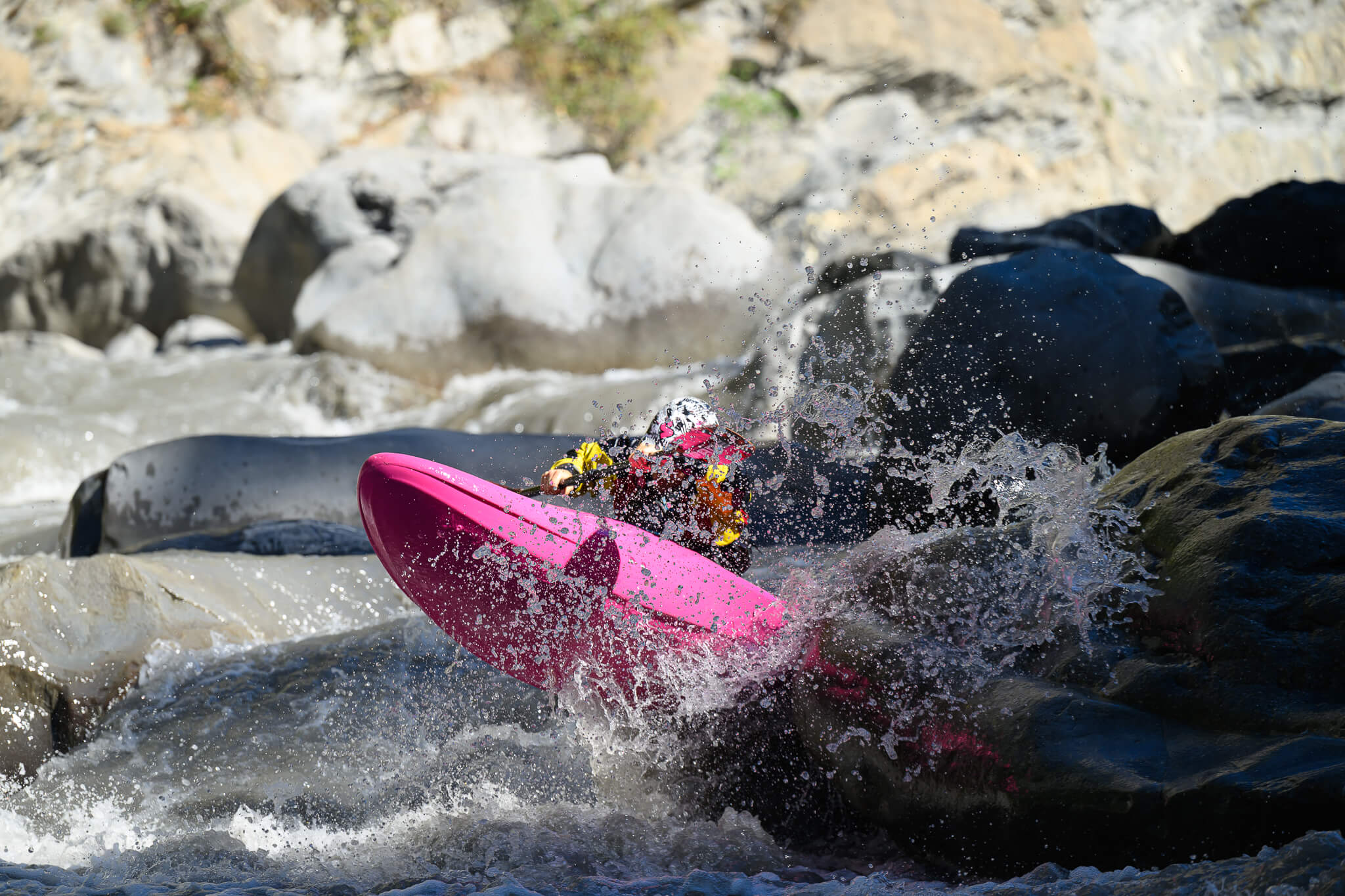 ubayak-05-race-day-landing-by-cedric-eyma A racer landing a drop in a pink kayak, spray exploding off the rock.